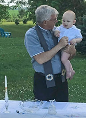 Jeff Sager holding a child during an outdoor baptism